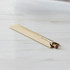 A Kraft paper pen sleeve in a beige shade, containing a silver pen with a wooden barrel, resting on a marble surface.