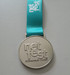 A silver medal with a turquoise ribbon featuring a logo and the text "net fest Sunshine Coast."