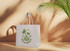 A light canvas bag featuring green palm tree graphics and a logo, set against a warm, minimalist background.