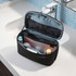 A black toiletry bag with a removable pouch, featuring various personal care items inside, displayed on a bathroom countertop.