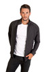 A man wearing a charcoal grey zip-up jacket over a white t-shirt, posing with hands in pockets. The jacket has a logo.