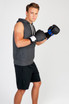 A man wearing a grey sleeveless hoodie, black shorts, and boxing gloves, posed for a promotional image.