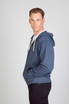 A man wearing a navy blue heather zip hoodie, standing with his hands in the pockets and smiling.
