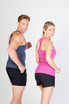 A blue athletic T-back singlet on a man and a pink athletic T-back singlet on a woman, both wearing black shorts.