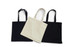 Three tote bags in black and cream, featuring long handles and a simple design, one bag in the front is cream.