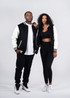 A black and cream varsity jacket featuring a logo, displayed on a man and a woman in casual attire.