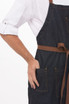 A denim bib apron in dark blue with a brown tie and pockets, featuring a hand resting on one of the pockets.
