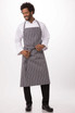 A chef apron in grey with white stripes, worn by a smiling man in a white shirt and black trousers.