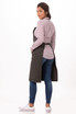 A Dorset Bib Apron in a dark colour, worn over a checked shirt, paired with blue jeans and white sneakers.