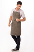 A man wearing a dark green Dorset Bib Apron with a front pocket, styled with a shirt and dark jeans.