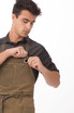A man adjusts a green Dorset bib apron, featuring pockets and a logo, while wearing a black shirt.