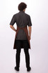 A brown Dorset Bib Apron worn over a black shirt, viewed from the back, featuring a logo.