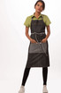 A denim bib apron in dark grey with a front pocket, worn over a green shirt and black leggings.