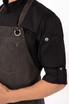A dark grey chef's bib apron worn over a black shirt, featuring a front pocket and a circular ring detail.