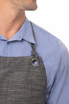 A grey bib apron with a ring detail on the neck strap, worn over a blue shirt.