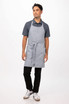 A grey bib apron worn by a man standing against a plain background, featuring a front pocket and ties.