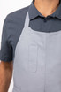 A grey Logan Bib Apron with a front pocket, worn over a patterned blue shirt.