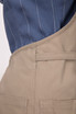 A beige Logan Bib Apron featuring pockets, worn over a blue pinstripe shirt, with a logo visible.