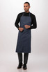 A dark blue bib apron is worn by a model, featuring a simple design and adjustable straps. It includes a logo.