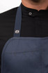 A dark navy bib apron with a logo and a pocket, worn over a black shirt.