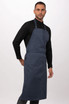 A dark blue bib apron worn by a model, featuring adjustable straps and a logo.