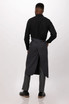 A black bib apron with a stylish back design, worn over grey trousers and black shoes. The apron has a logo on it.