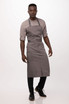 A grey bib apron worn over a light-coloured shirt, complemented by black trousers and shoes. The model stands confidently.
