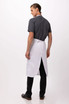 A man wearing a white bib apron over a grey shirt, viewed from the back with black trousers and shoes.