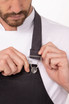 A man adjusts the strap of a black Boulder Bib Apron, featuring a silver attachment clip.