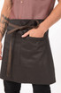 A dark brown bistro apron with a front pocket, tied at the waist and worn by a person with arm tattoos.