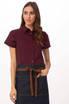 A woman models a maroon shirt paired with a denim apron featuring a brown tie belt. The apron has a simple design.