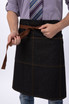 A dark denim apron with brown ties, worn by a person who is tying it around their waist.
