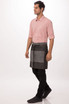 A man wearing a grey and dark grey Manhattan Half Bistro Apron over a light pink shirt and black pants, standing sideways.