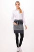 A woman wearing a denim bistro apron with a pocket, paired with a white shirt and black pants.