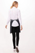 A woman in a white shirt and black pants wears a navy blue bistro apron, seen from the back.