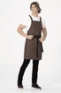 A brown cross back apron worn by a person, featuring straps and a waist tie, against a white background.