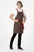 A brown cross back apron with red straps, featuring a waist tie and worn by a model.