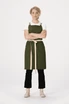 A model wears a green Lockharte Cross Back Apron over a white shirt, paired with black trousers and light-coloured shoes.