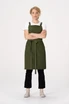A green cross back apron with a tie waist, worn over a white t-shirt, modelled by a standing woman with curly hair.