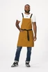 A man wears a mustard yellow Lockharte Cross Back Apron with a black waist tie, featuring a logo.
