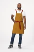 A man wearing a mustard yellow Lockharte Cross Back Apron with red straps and a matching tie, featuring a pocket.