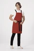 A red cross-back apron with black straps, worn by a model standing with hands on hips, featuring a logo.