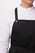 A black Largo Bib Apron worn over a white collared shirt, featuring leather straps and a clean design.