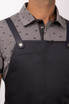 A dark navy bib apron features adjustable straps and a front pocket, worn over a patterned grey shirt.