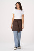 A woman models a brown Lockharte waist apron over a white shirt and blue jeans, featuring a tie at the waist.