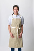 A lightweight beige cross-back apron with adjustable straps and a tied belt, featuring two front pockets.
