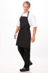 A black bib apron worn by a person, featuring adjustable straps and a functional design. The individual is standing confidently.