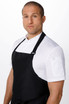 A black large bib apron worn over a white shirt, featuring a logo on the apron. The model stands with a neutral expression.