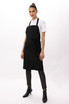 A black bib apron with adjustable straps, styled on a model wearing a white shirt and patterned pants.