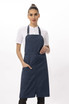 A navy blue bib apron is worn by a model, featuring a sleek design and pockets. It has a logo on it.